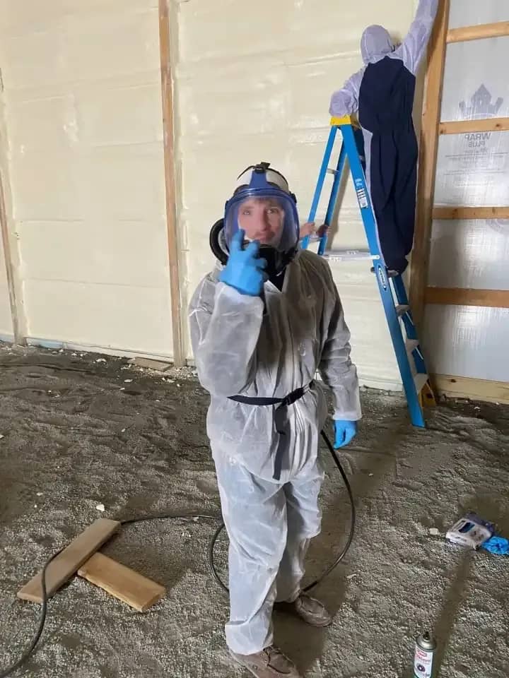 Hoosier Spray Foam installers in protective suits and respirators, one on a ladder, spraying foam on pole barn walls